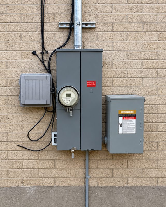 Meter base, service panel and transfer switch neatly mounted on a brick exterior